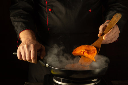 A chef expertly flips a vibrant orange ingredient in a sizzling pan. Steam rises, filling the air with enticing aromas, showing culinary expertise in a stylish kitchen environment.の写真素材