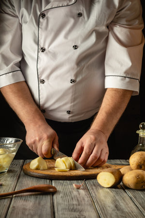 A skilled chef expertly chops potatoes on a wooden cutting board surrounded by fresh produce. The kitchen exudes a cozy atmosphere, enhanced by warm lighting and rustic decor.の写真素材