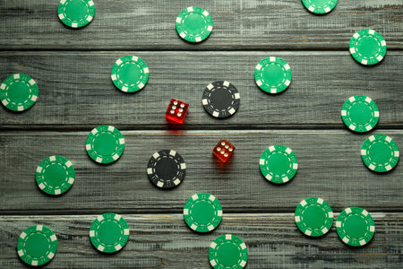 Colorful chips are scattered across a textured wooden surface, with a pair of red dice resting in...