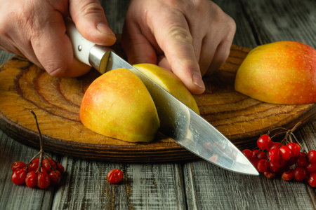 Hands skillfully cut ripe apples on a wooden cutting board, surrounded by vibrant red berries. The warm atmosphere evokes the joy of preparing a delicious snack.の写真素材