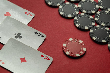 A close-up shot of an exciting card game featuring three aces and a set of poker chips on a red surface during an evening reception.の写真素材