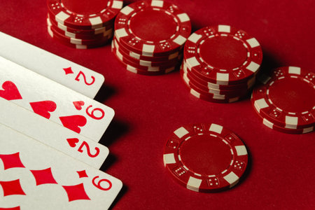 A close-up of red poker chips stacked next to four playing cards depicting pairs of twos and nines....