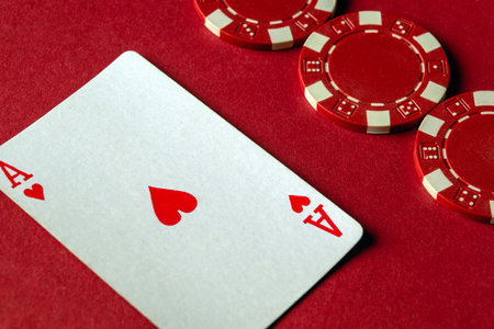 A red table showcases a playing card featuring an Ace of Hearts alongside several red poker chips, setting the mood for an exciting card game night.の写真素材