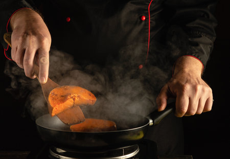A chef prepares colorful vegetables in a pan, skillfully using a spatula amidst rising steam. The warm ambiance of the kitchen creates an inviting atmosphere for cooking.の写真素材