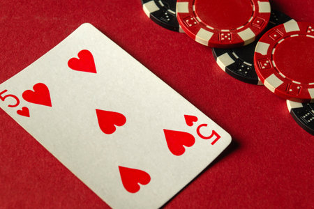 A five of hearts card lays on a red table next to various poker chips, capturing the excitement of a game night filled with strategy and competition among friends.の写真素材