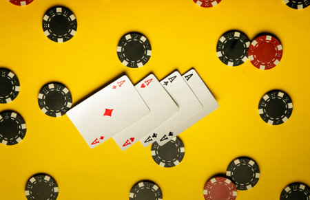Four aces are displayed on a bright yellow surface surrounded by an array of black and red poker chips, symbolizing excitement and competition in gaming.の写真素材