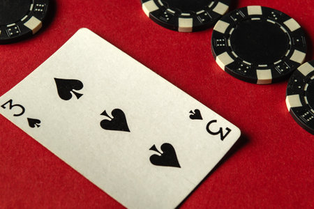 A game of poker is underway with players contemplating their next moves. A three of spades lies prominently on a red table surrounded by black and white chips, showcasing a competitive atmosphere.の写真素材