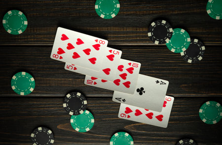 An exciting game of poker, with playing cards and green chips scattered across a wooden table. The atmosphere is lively and filled with anticipation and excitement.の写真素材