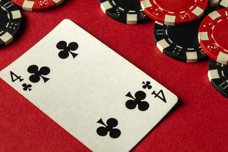 A four of clubs card is laid on red felt alongside various poker chips. The setting suggests an exciting casino atmosphere during a competitive poker game.の写真素材
