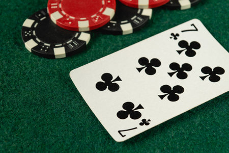 A close-up view of a playing card displaying the seven of clubs alongside various poker chips, set on a vibrant green felt surface during a lively gaming session.の写真素材