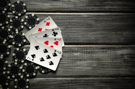 On a dark gray vintage table a successful combination of playing cards four of a kind or quads and black chips received from winning are laid out next to each other. A very successful game of poker.の写真素材