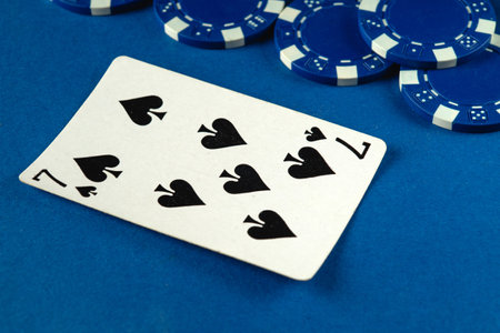 A seven of spades card lies flat on a vibrant blue surface, surrounded by blue poker chips, indicating an ongoing card game and excitement of competition.の写真素材