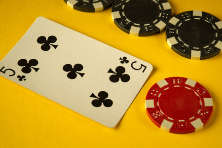 A five of clubs playing card sits alongside various casino chips on a vibrant yellow surface, creating a lively gaming atmosphere. The contrast of colors enhances the excitement.の写真素材