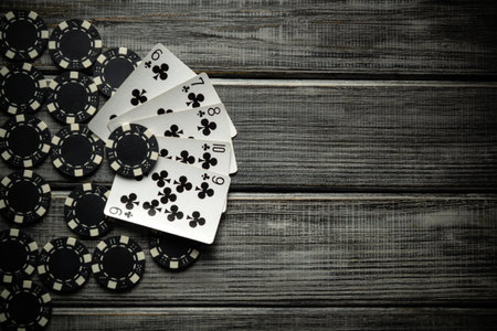 On a gray vintage table, a successful combination of straight flush playing cards and black chips from winning are laid out side by side. Luck in the game of poker depends on the mood.の写真素材
