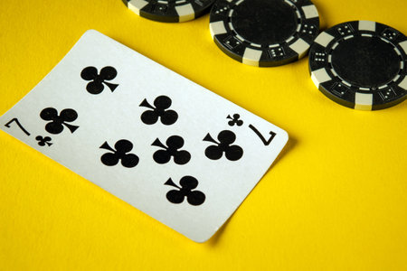 Seven of clubs card placed on a vibrant yellow surface alongside several black casino chips, creating a lively atmosphere for a game night among friends.の写真素材