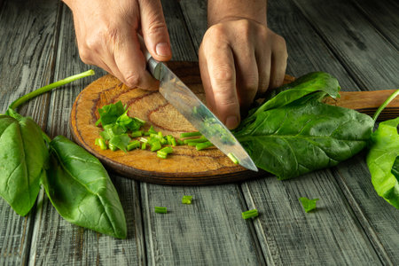 A pair of hands skillfully chop fresh green herbs on a wooden board. The kitchen atmosphere is warm and inviting, emphasizing home cooking.の写真素材