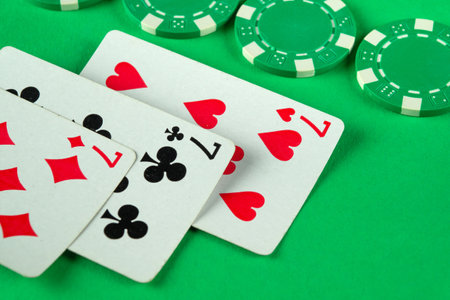 Green chips and playing cards with a combination of three of a kind or set are randomly laid out on a poker table. The concept of a lucky win in a club.の写真素材