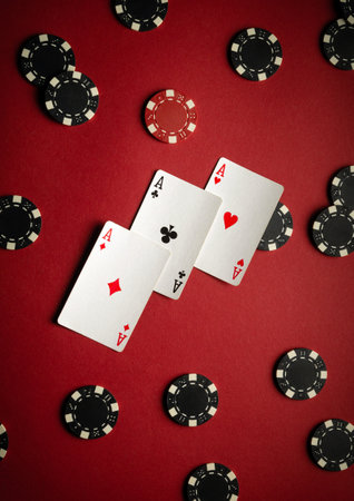 Three aces are displayed on a red table surrounded by black and red poker chips, indicating an...