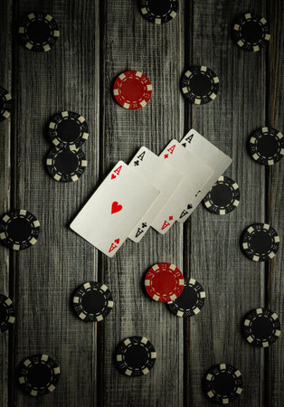 A winning hand of four aces is fanned out on a rustic wooden table surrounded by poker chips. The setting suggests an intense poker game filled with excitement and strategy.の写真素材