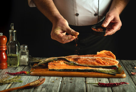 A chef seasons fresh salmon fillets with various spices in a rustic kitchen, showcasing culinary techniques and attention to detail during meal preparation.の写真素材