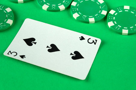 A three of spades card lies on a vibrant green felt surface surrounded by various poker chips, indicating an exciting late-night poker game taking place.の写真素材