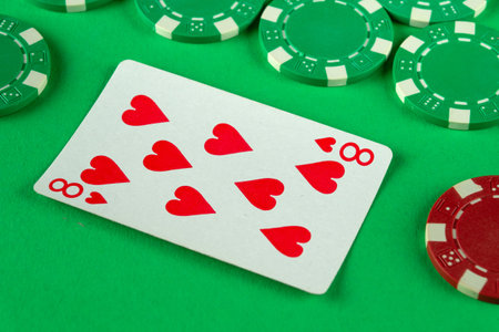 A vibrant green felt gaming table displays an eight of hearts alongside several poker chips, suggesting an exciting casino environment for players enjoying a game.の写真素材