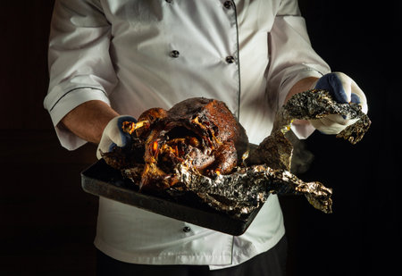 A chef proudly holds a tray displaying a beautifully roasted chicken wrapped in foil, revealing a rich, flavorful dish ready for a festive meal. The kitchen ambiance adds to the culinary excitement.の写真素材