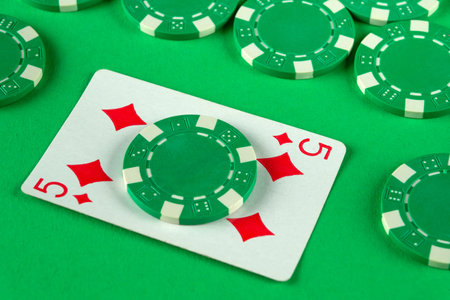 Various green poker chips are scattered around a playing card showing a five of diamonds, creating a vibrant casino atmosphere ideal for game night.の写真素材