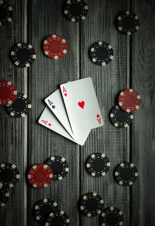 Three playing cards showing aces are placed on a wooden table surrounded by red and black poker chips, highlighting a winning moment in a late-night poker game.の写真素材