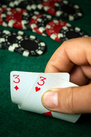 Poker enthusiast prepares for a critical moment in the game, holding a pair of threes in one hand while various colorful chips are scattered around the green felt table.の写真素材