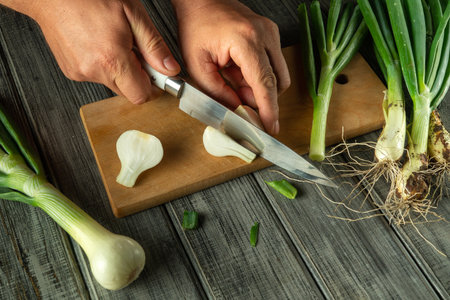 Hands skillfully cut fresh green onions on a wooden board. The vibrant colors of the vegetables pop against the rustic kitchen setting, perfect for meal prep.の写真素材