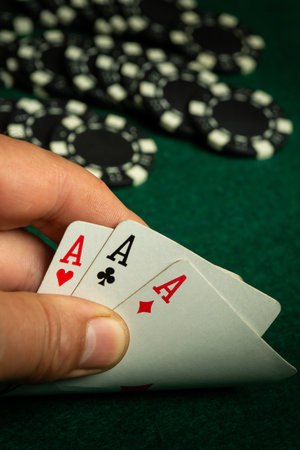 A player holds three aces in their hand while surrounded by poker chips on a green felt table. The...