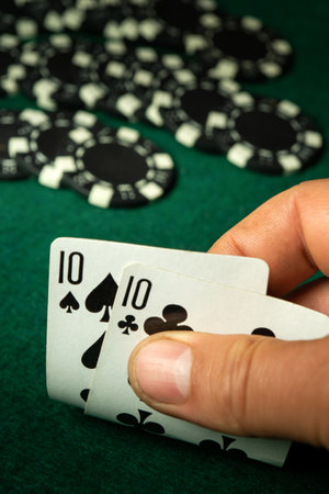 A player reveals a pair of tens in a card game at a casino table, surrounded by black and white poker chips on a green felt surface. The action captures the excitement of gameplay.の写真素材