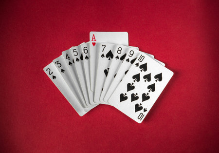 A deck of cards is displayed on a rich red surface, highlighting the numbers and the ace of hearts. The composition emphasizes the spade suit, creating a playful atmosphere.の写真素材