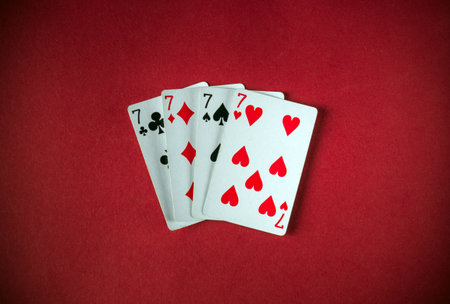 Four playing cards featuring the seven of hearts, seven of spades, and seven of diamonds are arranged on a vibrant red cloth, creating an engaging display for card games or tricks.の写真素材