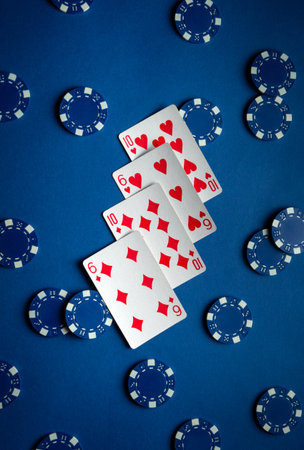 A set of playing cards displaying hearts and diamonds lies in a fan shape on a dark blue surface. Blue poker chips are scattered around, indicating an engaging card game in progress.の写真素材