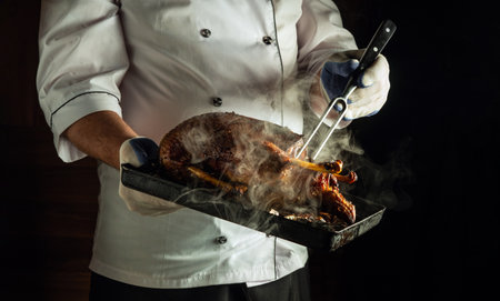 A chef in a white uniform holds a black tray filled with sizzling grilled meat. The steam rises, indicating the dish is freshly prepared and ready to be served in a kitchen.の写真素材