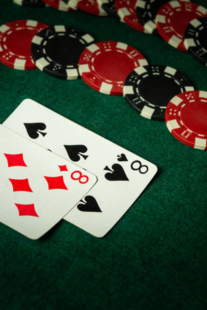 Two playing cards, an eight of hearts and an eight of spades, lie on a green felt surface with red and black poker chips scattered around. The atmosphere suggests a casual gaming night with friends.の写真素材