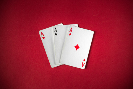 Three ace playing cards rest on a bright red felt surface, signaling a potential winning hand during a friendly card game. The atmosphere is casual and engaging.の写真素材