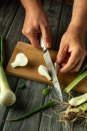Hands skillfully cut fresh green onions on a wooden cutting board. The kitchen is filled with vibrant produce and earthy textures, enhancing the cooking atmosphere.の写真素材