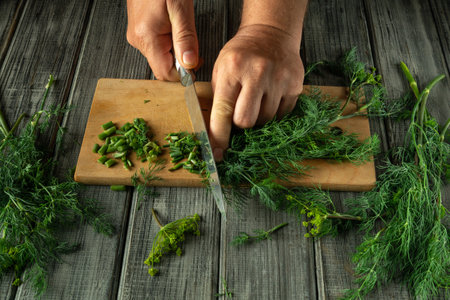A person finely chops green herbs on a wooden board, surrounded by freshly picked greenery. Natural light enhances the vibrant colors of the herbs and wood.の写真素材