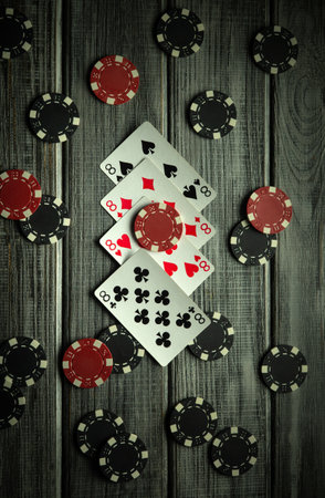 A collection of playing cards featuring four eights are scattered among black and red poker chips on a vintage rustic wooden surface.の写真素材