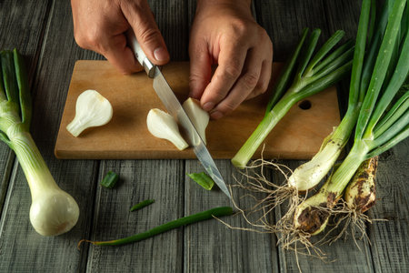 A pair of hands is trimming fresh green onions on a wooden cutting board. The kitchen exudes a warm atmosphere, making the food preparation inviting and homely.の写真素材