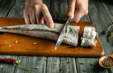 Hands skillfully fillet a fresh fish on a wooden cutting board, surrounded by spices and herbs. The...