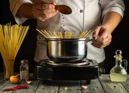 A chef prepares pasta on a stovetop, holding a wooden spoon. Fresh ingredients like garlic and onions are nearby, creating a warm atmosphere in the kitchen.の写真素材