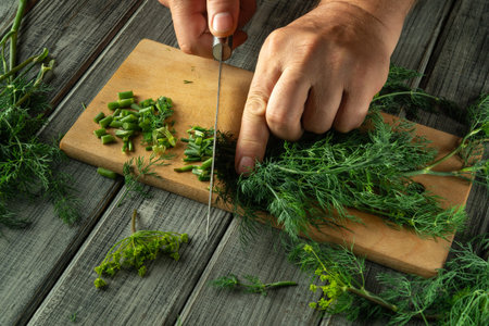 Hands are skillfully chopping fresh dill on a wooden cutting board. Surrounding the board are vibrant herbs, showcasing a culinary preparation moment in a cozy kitchen.の写真素材