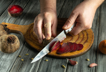 In a rustic kitchen, hands skillfully slice vibrant beets on a wooden cutting board while garlic cloves and spices create a flavorful atmosphere nearby.の写真素材