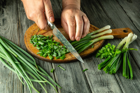 Hands skillfully chop scallions on a wooden board, surrounded by fresh green onions and herbs in a warm, rustic kitchen during daylight hours.の写真素材