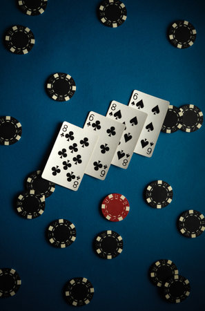 Cards displaying two sixes and an eight from the clubs suit are laid out among poker chips on a blue...