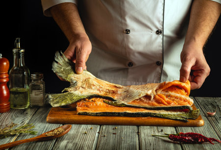 A chef skillfully fills fresh salmon, showcasing vibrant colors and textures. Various herbs and...